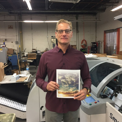 John Patrick Publishing Co. CEO John Hartmann holds up a proof that was printed on an HP T Series PageWide inkjet web press and then finished near-line on JPPC&rsquo;s IBIS Smart-binder SB-3 Plus HS saddle stitcher (in background).